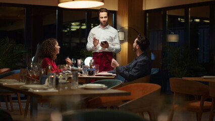 Restaurant waiter taking order serving romantic couple on evening dinner date.