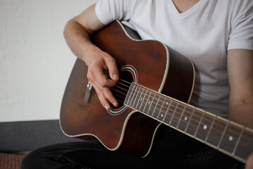 Obraz na płótnie Canvas A man in a white T-shirt, playing guitar at home.