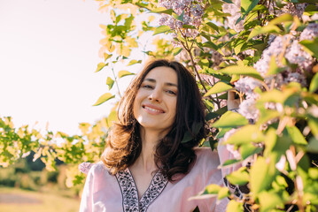 horizontal portrait of young beautiful female standing near the blossoming lilac tree wearing vyshyvanka - ukrainian national clothes. 