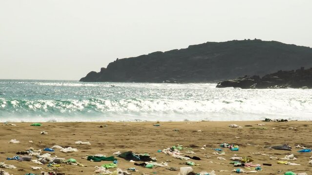 ocean waves crashing in to dirty polluted plastic trash waste sandy beach, zoom out on landfill garbage natural spot on seascape coastline