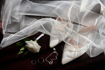 Close up of white women shoes, two golden wedding rings, boutonniere and veil on chair, copy space. Wedding concept. Top view, flat lay