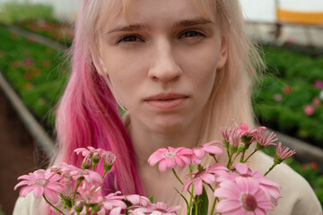 Obraz na płótnie Canvas Young woman with pink and blond hair holding pink flowers in garden