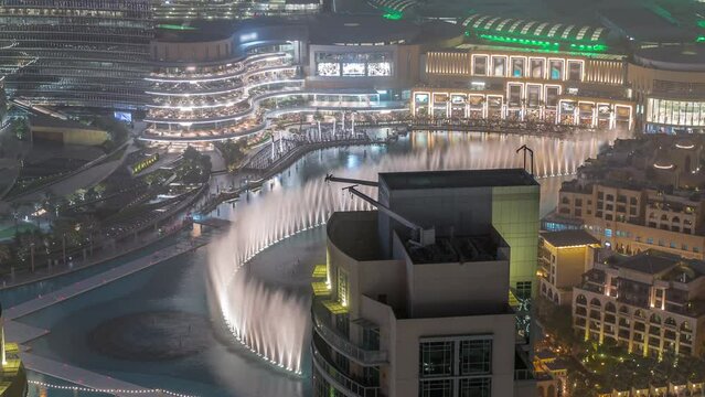 Dubai promenade singing fountains on the background of architecture with raditional houses in old town aerial timelapse. People watching show near shopping mall