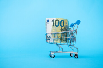 shopping cart with one hundred euro banknote on blue background Buying currency. Currency exchange....