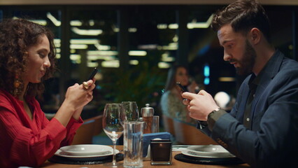 Digital couple surfing phone on restaurant dinner date. Social media concept.