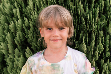 portrait face of candid happy little kid boy of five years old with problem allergic skin and long blond hair and green eyes on background of green plants during a summer vacation travel