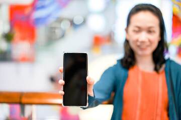 Black screen of mobile in Asian woman hand with blur face in department store background. For mock up website or application on smart phone. Clipping Path.