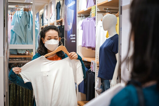 Young Asian Woman Try size T Shirt in front of the mirror in Cloth Fashion Shop.