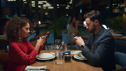 Multiethnic partners searching phone device on fancy restaurant dinner date. 