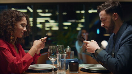 Multiethnic couple texting mobile phone in fancy restaurant. Dinner date concept