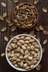 Pistachos con cáscara y pelados en un bol sobre una mesa de madera oscura.
