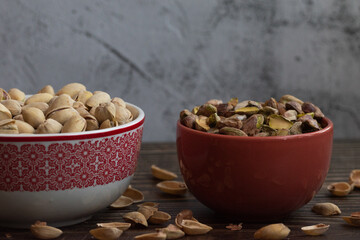 Pistachos con cáscara y pelados en un bol sobre una mesa de madera oscura.