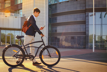 Young businessman with bicycle and smartphone on city street