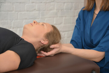 Medical treatment concept: brown-haired woman lying on massage table and having osteopathy treatment session at physiotherapy clinic.

Doctor osteopath hands doing physiological therapy for patient.