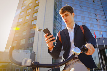 Young businessman with bicycle and smartphone on city street - obrazy, fototapety, plakaty