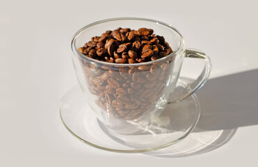 Glass cup full of coffee beans with sunlight and shadow on white backgraund close-up