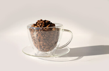 Glass cup full of coffee beans with sunlight and shadow on white backgraund