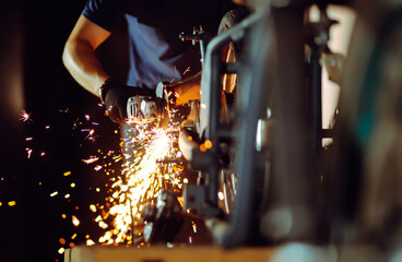 The hands of the master  with a grinder. metal works in the workshop close up. Sparks in metalworking.