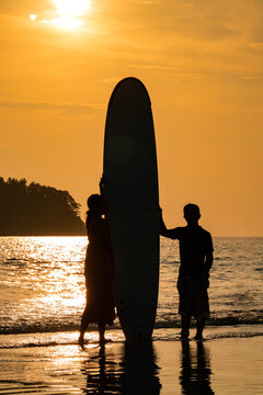 Art Silhouette Smart Asian Couple  Man and Woman, a romantic shot with Standed Surboard on beach with sunset behind them.