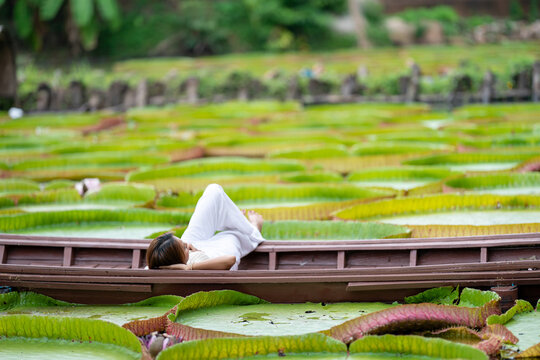 Asian Girl is lying down on the new vintage wood boat on the Lily Lotus Leaf pond at outdoor field.
