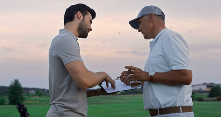 Two golfers communicate outside on sunset fairway. Golf group talk in sportswear