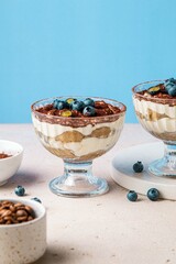 Homemade tiramisu with blueberries in glass jars. Traditional unbaked Italian dessert on blue background. Coffee and mascarpone cream cake. Copy space. Selective focus.