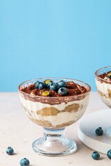 Homemade tiramisu with blueberries in glass jars. Traditional unbaked Italian dessert on blue background. Coffee and mascarpone cream cake. Copy space. Selective focus.