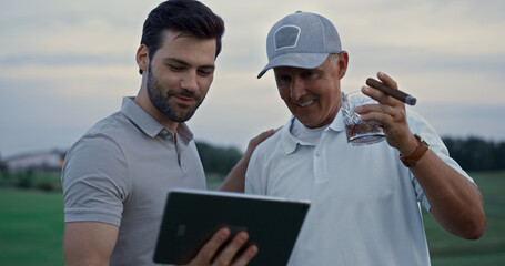 Smiling men calling online video holding tablet on golf course. Wealthy concept.