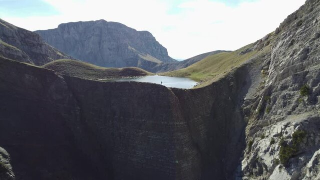 Aerial drone video from iconic and beautiful lake Drakolimni of Tymfi mountain, man stay on edge of cliff, Vikos National Park, Zagori, Greece