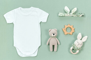 White baby bodysuit for mock-up on a pastel green background with crocheted teddy bear and rabbit...