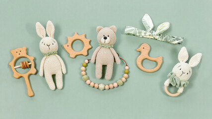 Children's toys on a green mint background. Wooden and knitted baby handmade toys in eco style for a banner. Infant baby toys concept. Wooden rattles, crocketed teddy bear and teething beads top view. - Powered by Adobe
