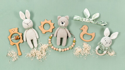 Baby infant toys background. Knitted bunny, handmade teddy bear and wooden teethers for banner on a mint green background. Wooden rattles, cute headband and raffia clouds for a cute baby banner.