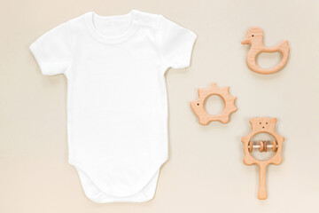 Baby clothes mockup with wooden teethers on pastel brown background in eco style. Handmade wooden toys and rattles for mockup with white baby bodysuit.