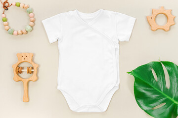 Eco friendly mockup with white wrap bodysuit and tropical monstera leaf on a pastel brown background. Teething beads and cute wooden toys for baby clothes mockup.