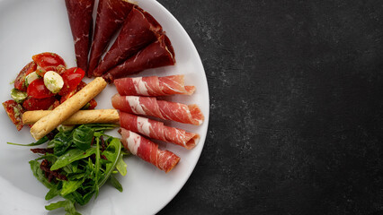 Meat appetizer with vegetable salad, arugula and grissini. Antipasti