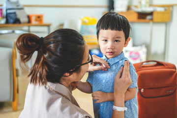 Mother help dress son fasten buttons. Woman fixing young boy's dress. Young mother adjusting son's shirt collar while living in the room.