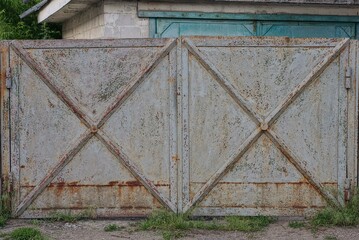one old gray closed metal gate in brown rust on the rural street