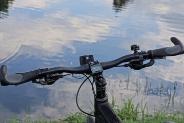 Fototapeta na wymiar part of a sports bike with a black bicycle handlebar in green grass on the shore of a lake near gray water