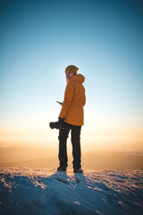 Traveller in a distinctive yellow jacket stands on top of a hill in the Polish Beskydy Mountains at sunset, enjoying the moment. Real people in winter ice environment