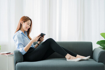 Obraz premium beautiful asian woman sitting on the sofa with a tablet At home, in the living room, video call with friends over the Internet.