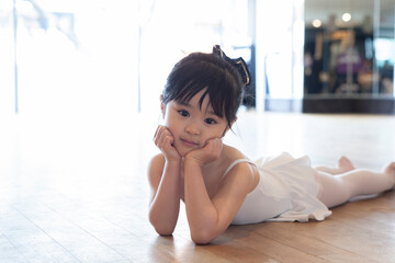 床に寝転がって頬杖をつくバレリーナの幼い女の子