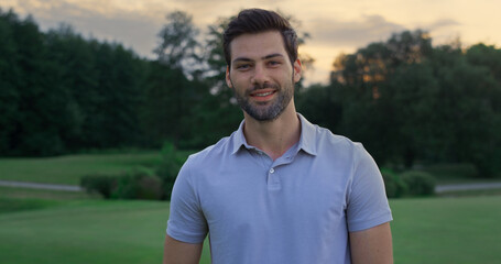 Happy model smiling outside. Handsome sportsman standing on golf course sunset.