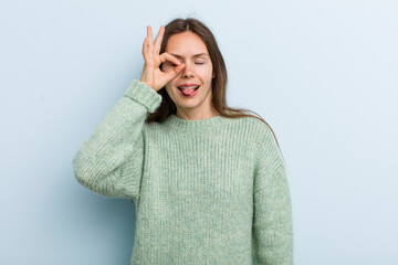 young adult pretty woman smiling happily with funny face, joking and looking through peephole,...
