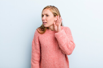 young adult blonde pretty woman looking serious and curious, listening, trying to hear a secret...