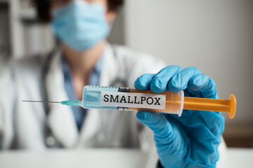 Syringe smallpox vaccine syringe doctor's blurred face. Mandatory vaccination during dangerous epidemic of influenza smallpox. Doctor holds syringe with vaccine. A new virus is spreading in a pandemic