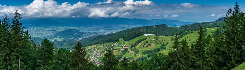 Panorama vom Rheintal mit Feldkirch und den umliegenden Dörfer, von Viktorsberg aus fotografiert. Schweizer Berge und Lichtenstein im Hintergrund. Sommertag mit Sonne und Wolken