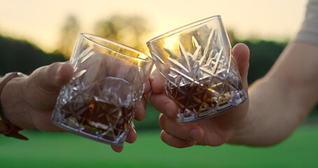 Friends toast glasses outdoors. Two men clinking drinks together on sunset field