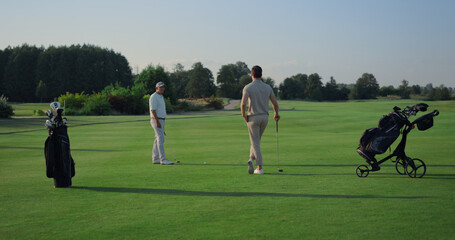 Active men enjoy golf on course field. Two golfers teeing play sport outside.