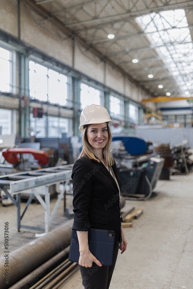 Wall mural portrait of female chief engineer in modern industrial factory holding tablet.