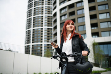 Portrait of businesswoman commuter on the way to work with bike, using smartphone, sustainable lifestyle concept.